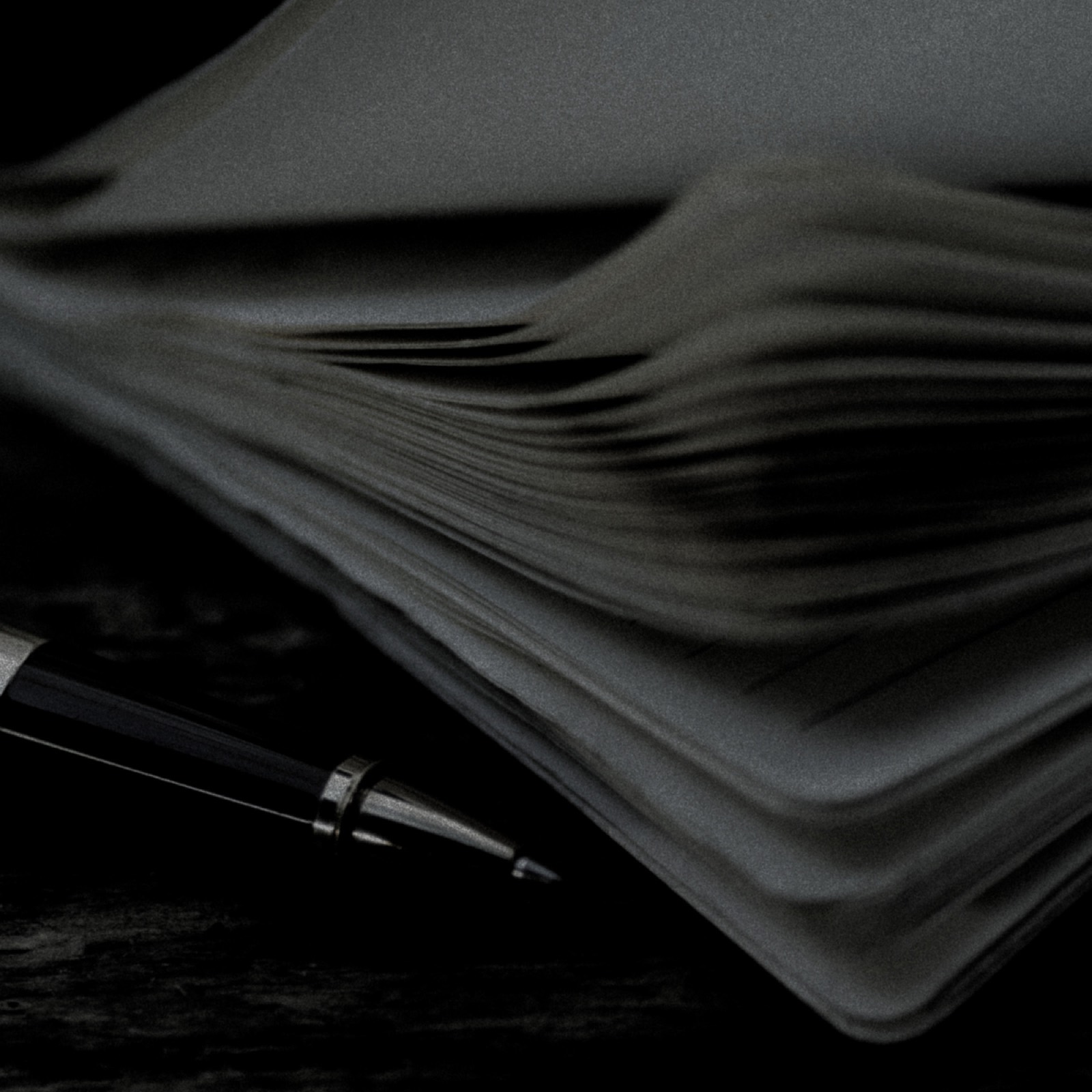 A worked notebook and pen in low light, black and white